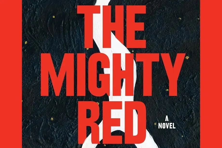 Book cover with bold red text reading "THE MIGHTY RED" across the center, and smaller white text beneath reading "A Novel." The background is a textured dark surface with small golden flecks, bisected vertically by a thick, jagged white line.